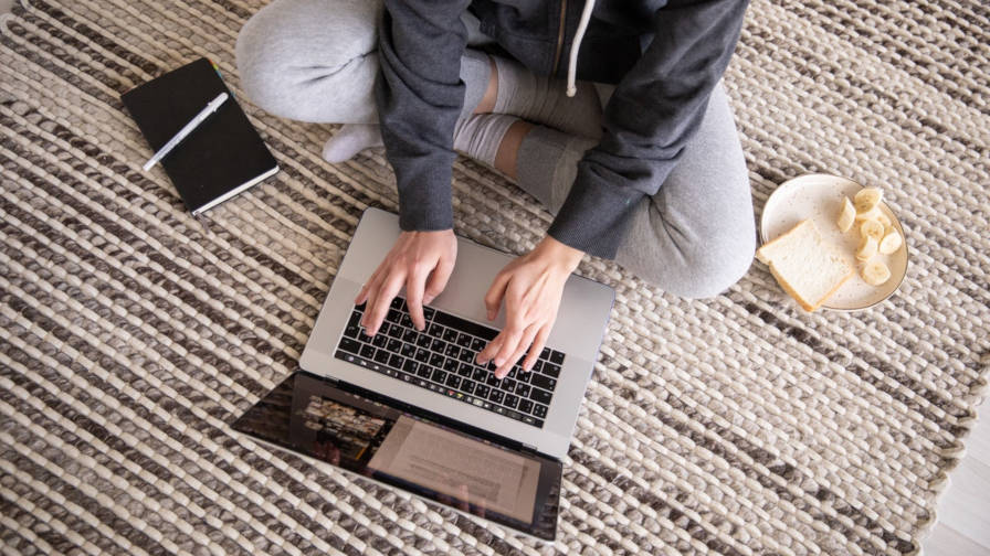 Person sitting in sweats on the floor and typing on a laptop.