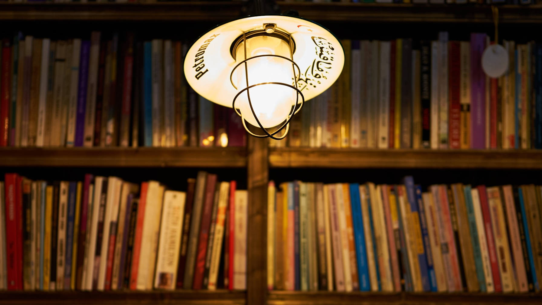 Shelves filled with books with a hanging light in front, illuminating them.
