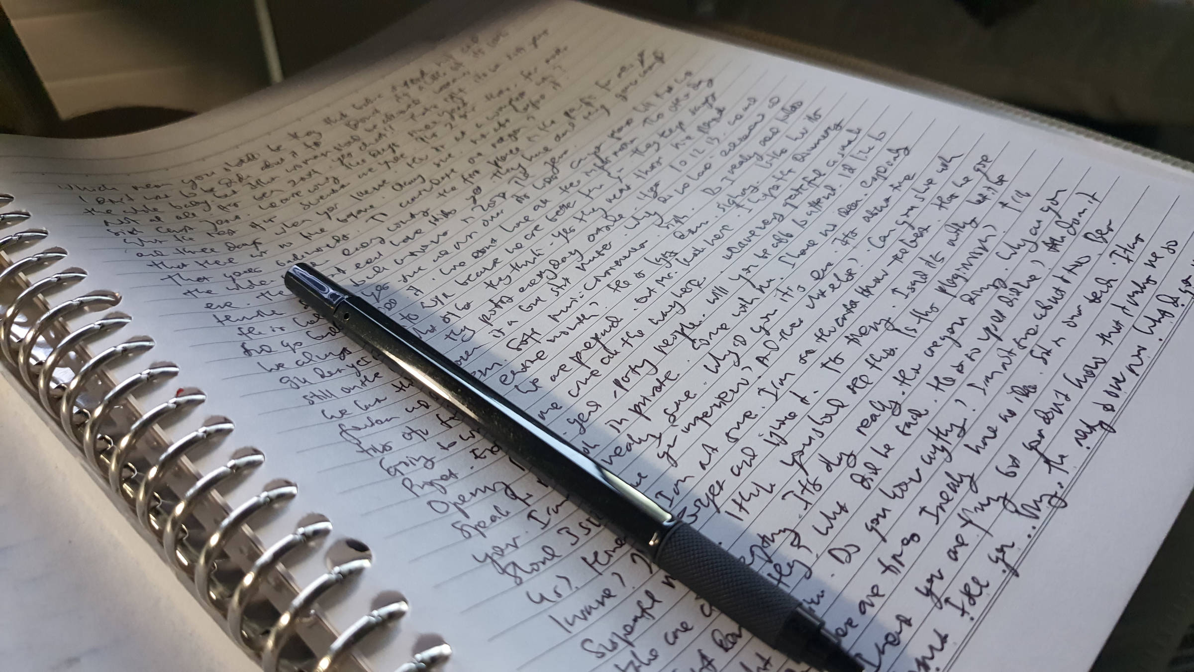 Texto escrito em um caderno de papel encadernado em espiral com uma caneta em cima dele.
